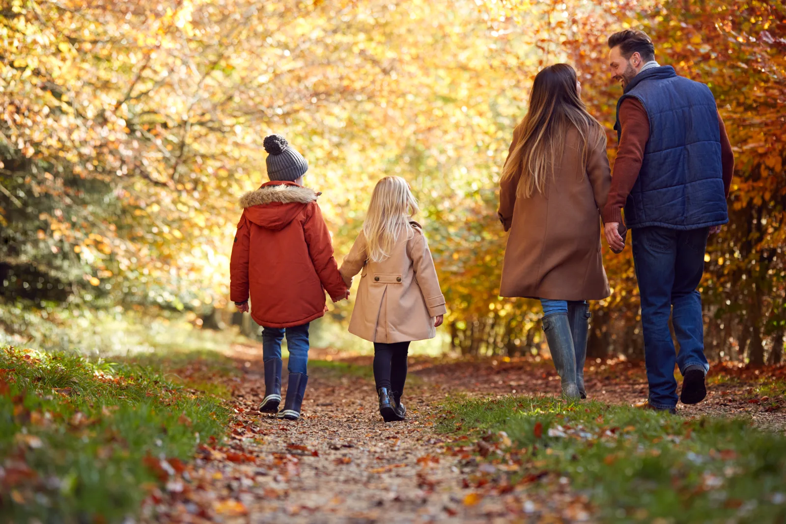 A family walking together along the same path through autumn trees, soft daylight