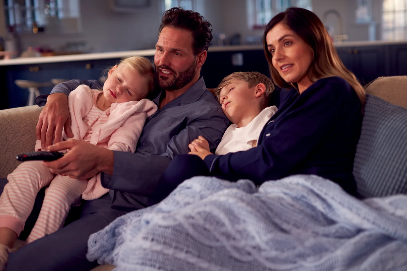A family on a couch under blankets watching a film together in warm low light