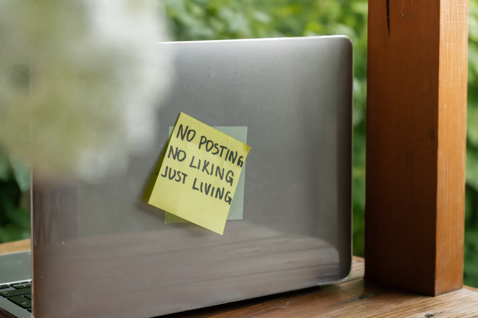 A paper note that reads no posting, no liking, just living, on a desk