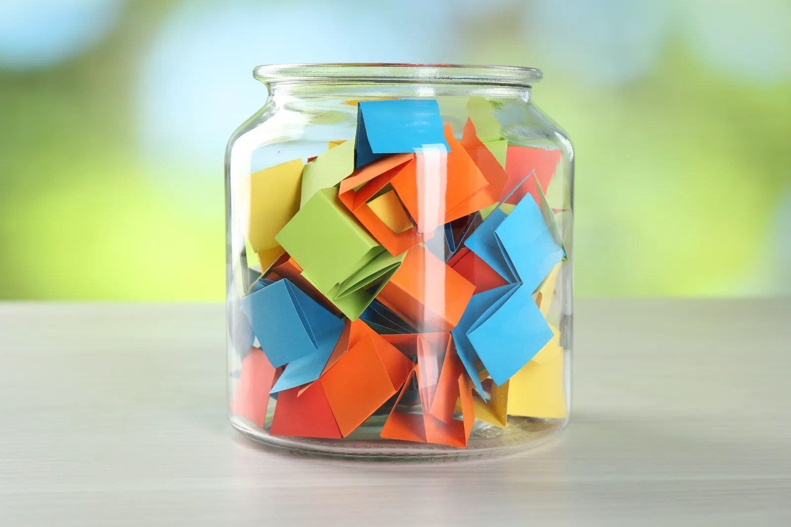 A glass jar filled with folded paper notes on a windowsill in warm light