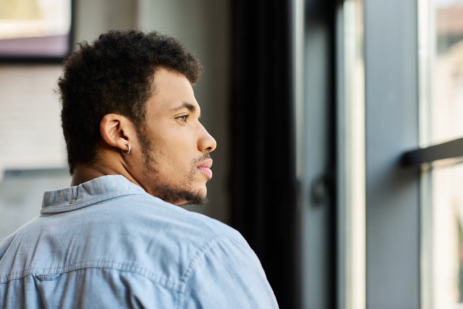 A person looking out a window with a calm, thoughtful expression in warm morning light
