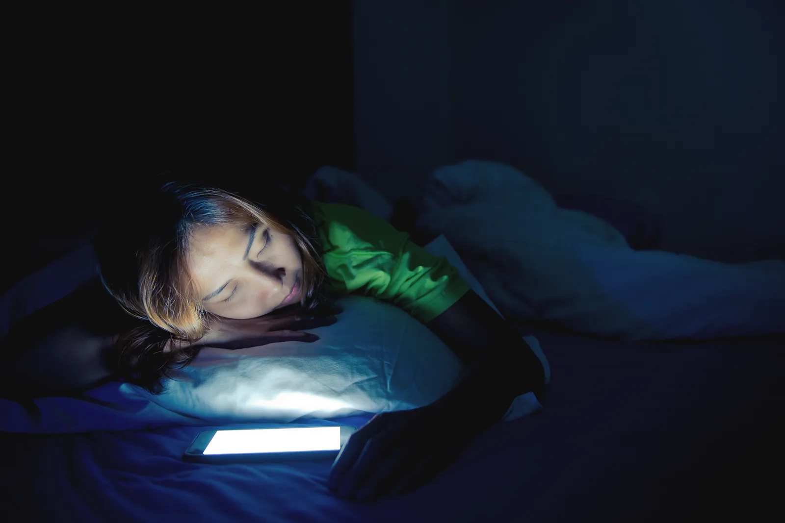 A dim bedroom at night with the soft glow of a phone screen on the pillow