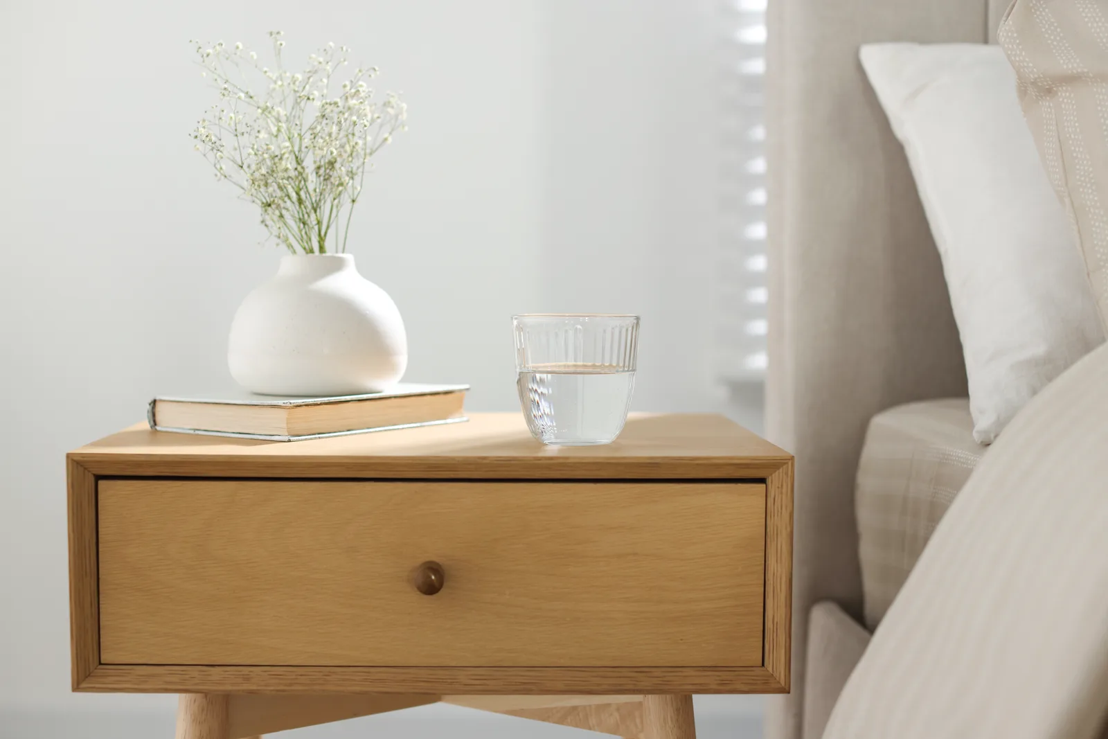 A calm nightstand with a book, a lamp, and an alarm clock, no phone in sight