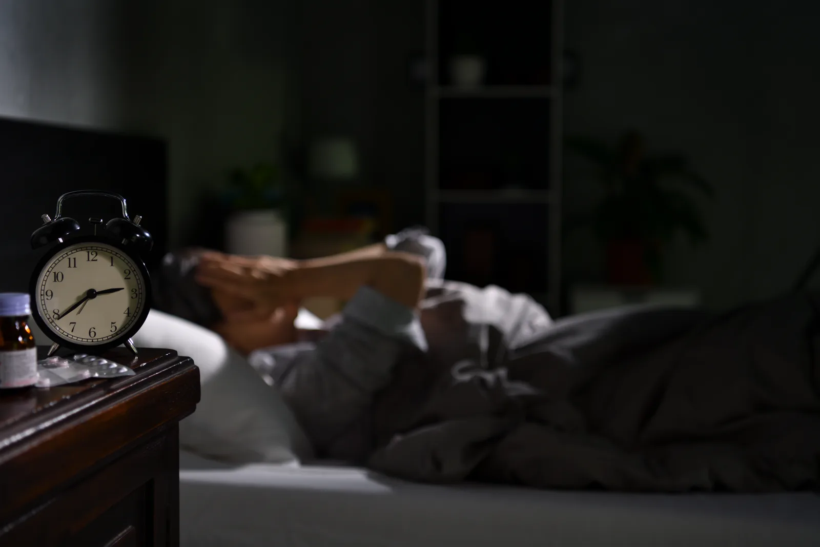 A person lying awake in bed at night, eyes open in the dark, looking anxious